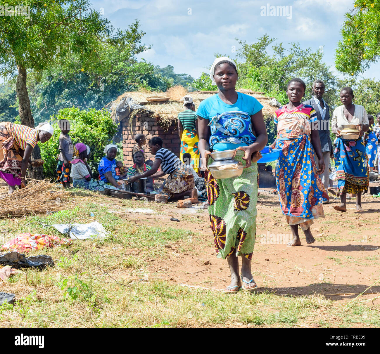 Les jeunes femmes à pied transportant de bols de gruau de maïs dans leurs mains dans un village du Malawi Banque D'Images