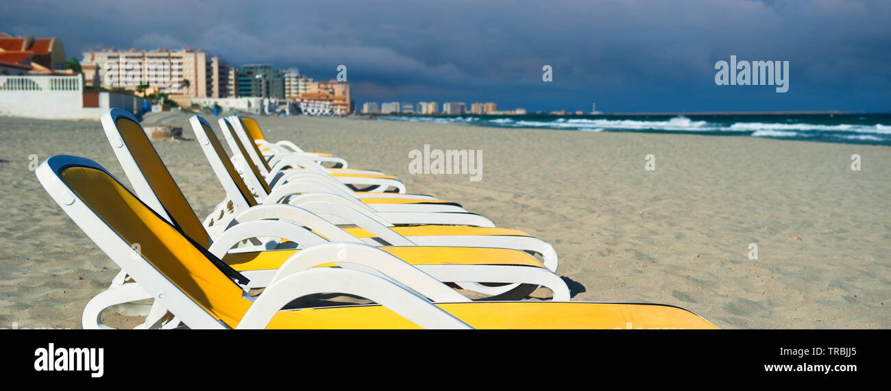 Image horizontale vue rognée jaune bleu chaises longues vides chaises longues dans une rangée sur la plage de sable, la Manga del Mar Menor bord de mer. Espana Banque D'Images