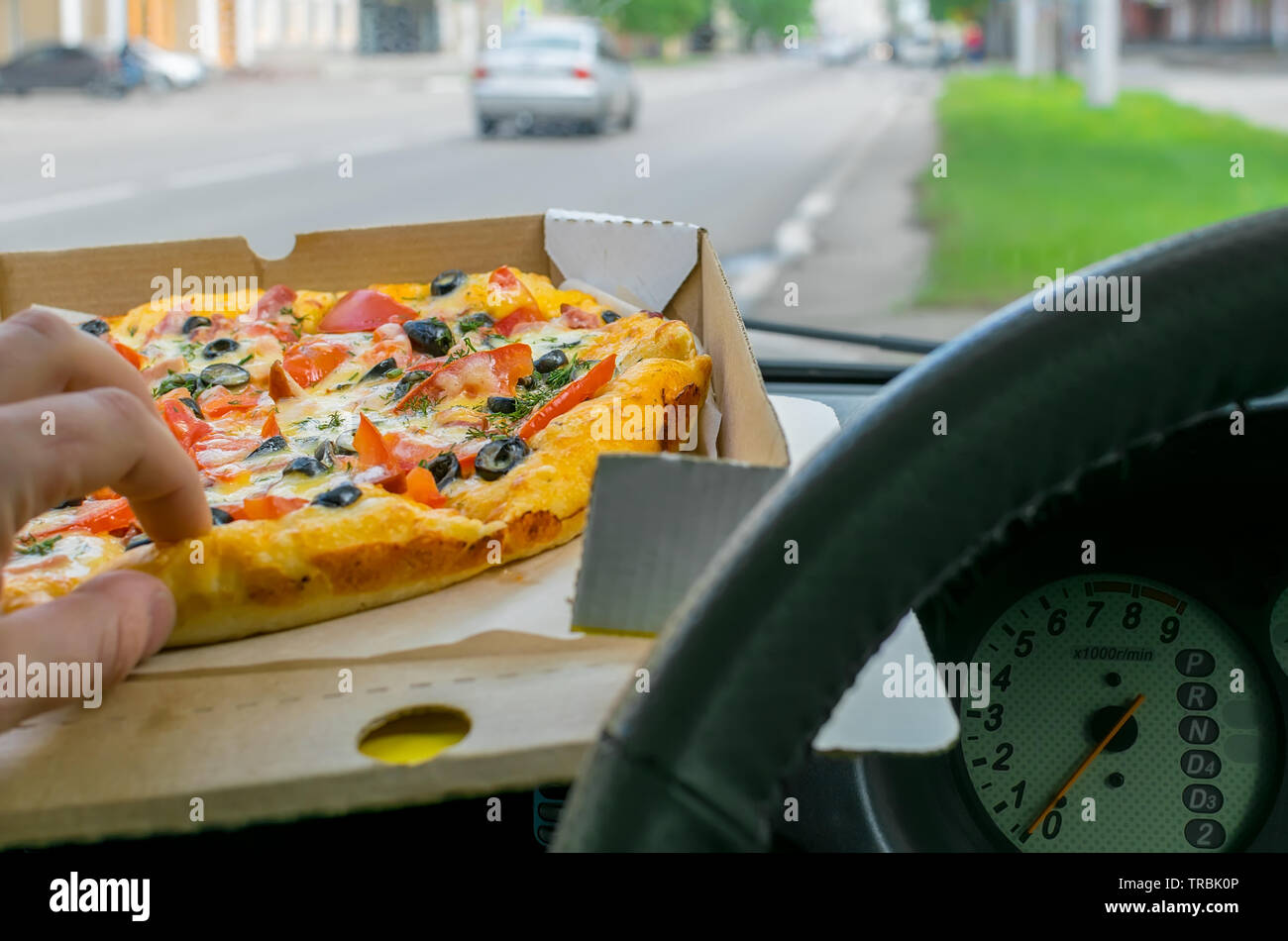 Le pilote part prend un morceau de pizza, l'emballage de ce qui se trouve sur le pare-brise de la voiture garée sur l'arrière-plan de la chaussée de la ville Banque D'Images