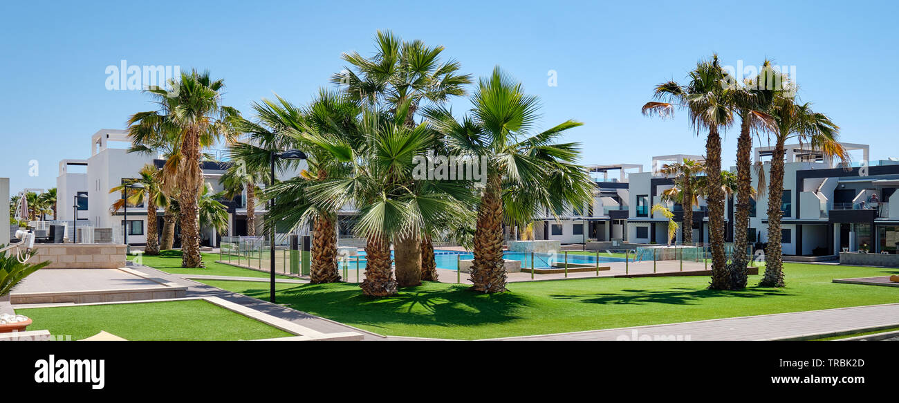 Jardins de palmiers à l'intérieur de l'urbanisation fermée avec pelouse verte piscine maisons modernes de jour d'été. Nouvelle propriété en Espagne, aucun peuple Banque D'Images