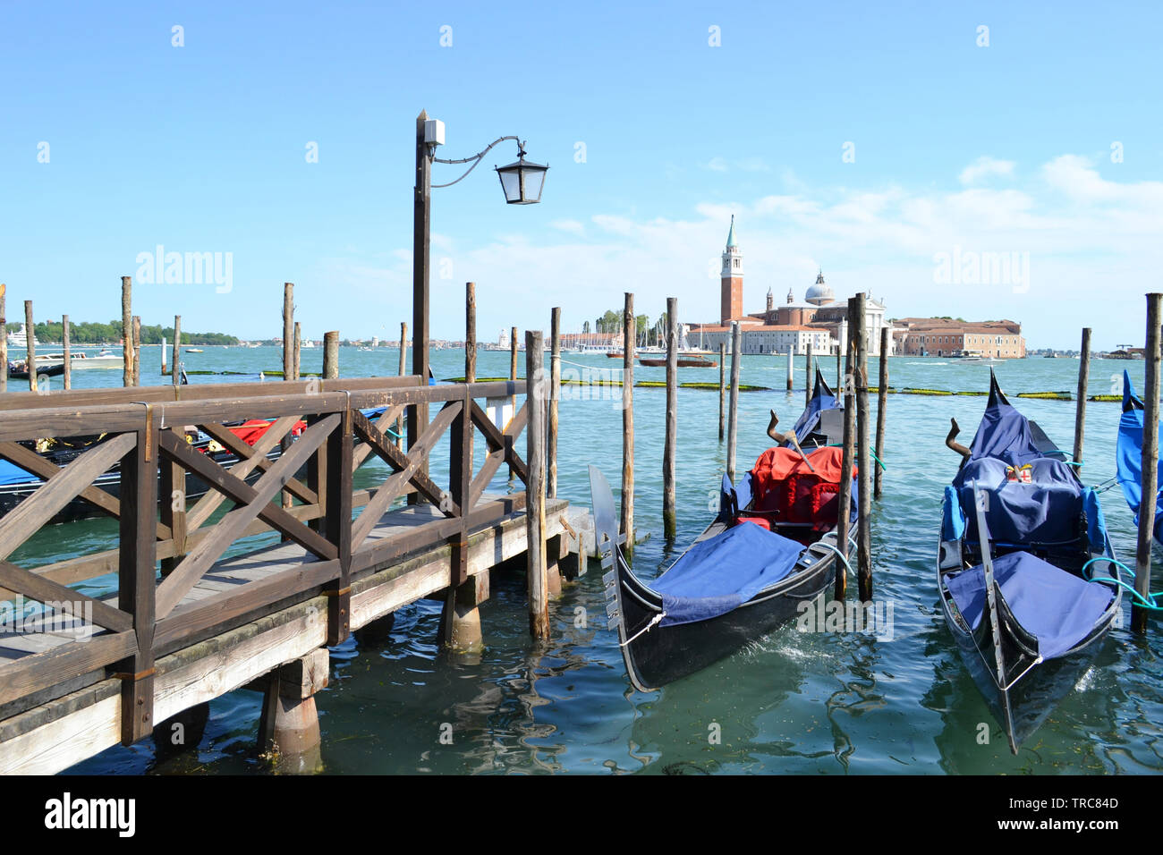 Une vue panoramique sur la lagune de Venise, San Giorgio Maggiore island, deux gondoles ancrées à des poteaux en bois, près de l'embarcadère en bois en journée ensoleillée. Banque D'Images