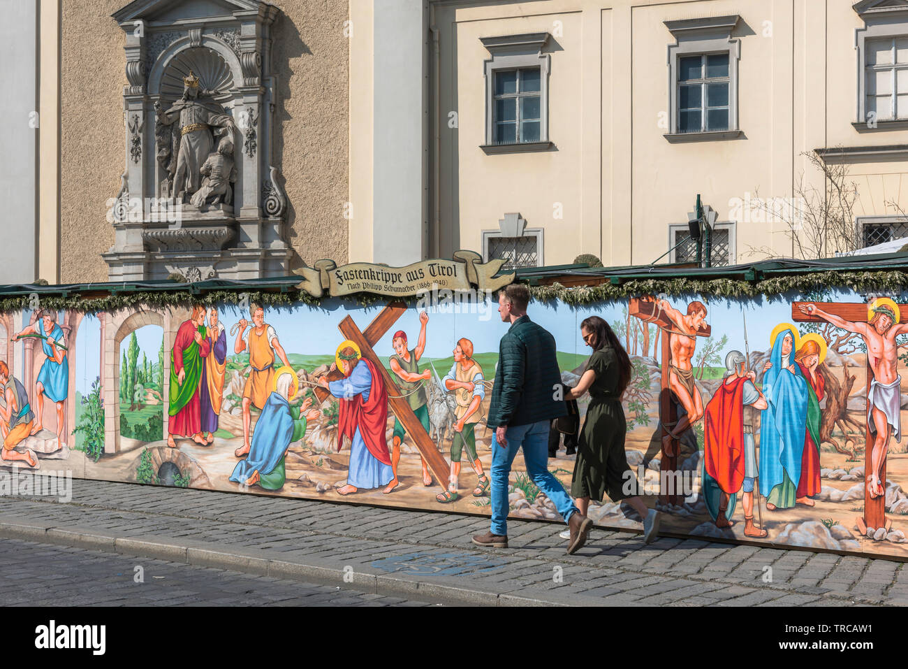 Pâques vienne, vue d'un jeune couple en train de marcher passé une illustration colorée de la Passion du Christ à côté de la Schottenkirche dans le centre de Vienne. Banque D'Images