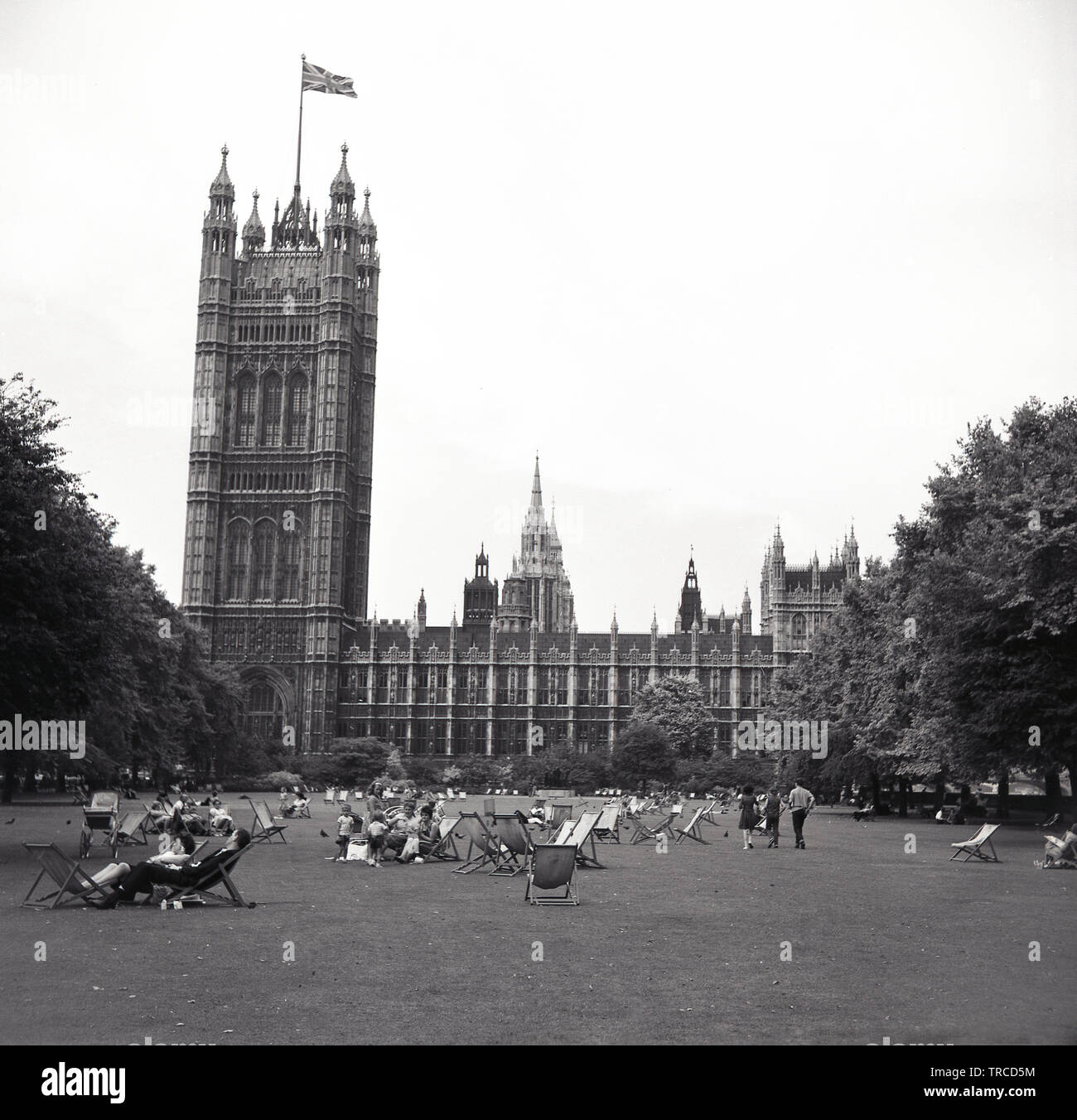 1960s, historique, vue sur les jardins de la tour Victoria avec des personnes dans des transats assis sur l'herbe, Westminster, Londres, Angleterre, Royaume-Uni. Le drapeau de l'Union Jack survole la tour, située à côté du palais de Westminster. Banque D'Images