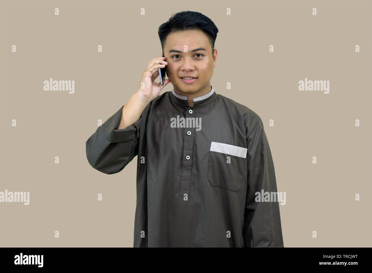 Portrait de l'homme posant dans la jeunesse musulmane tenue musulmane debout devant la caméra, en utilisant un téléphone intelligent isolé dans brown Banque D'Images