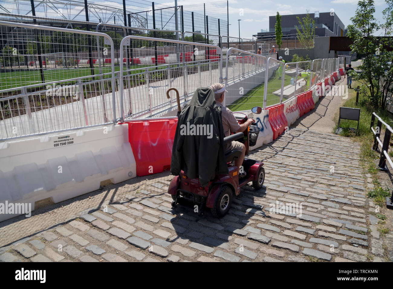 Personne âgée handicapée scooter durs travailleurs depuis la construction de nouveaux logements de luxe,un campus de l'université de la mode, des boutiques et des bureaux le long de canal Banque D'Images