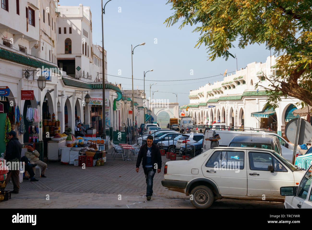 Rue principale de Moulay Idriss, un jour ensoleillé, avec des maisons blanches, des boutiques, des bars et des voitures en stationnement. Moulay Idriss Zerhoun, le Maroc. Banque D'Images