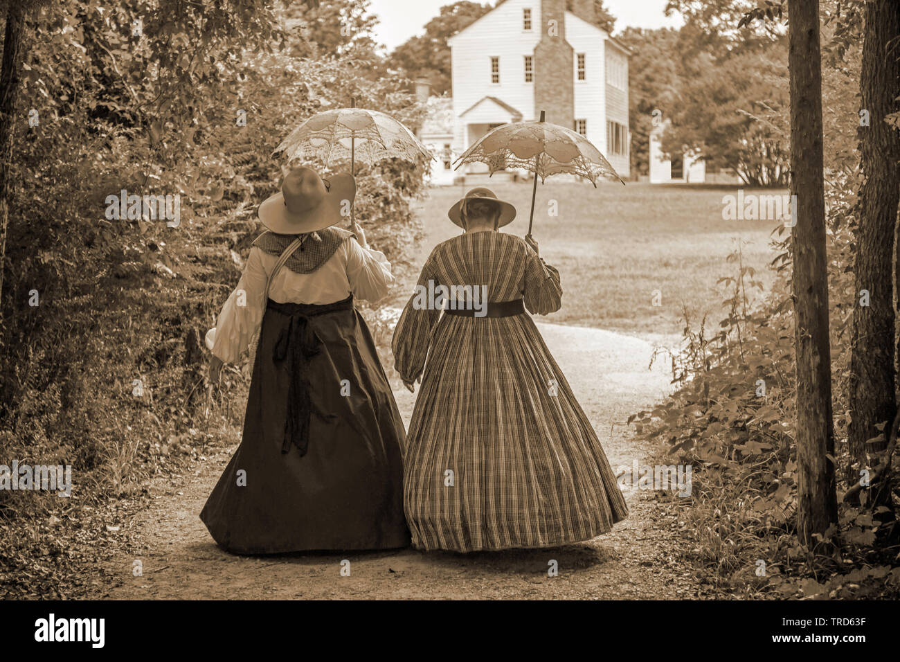 Deux femmes portant des robes d'avant à pied avec des parasols sur les motifs d'une plantation de Caroline du Nord historique. Banque D'Images
