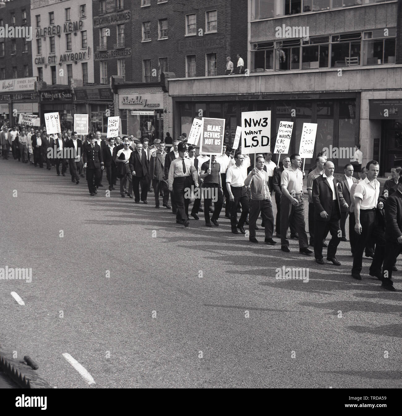 1964, des poseurs du Royal Mail, historiques et en grève, des membres de l'Union des travailleurs de la poste (UPM) se promène dans un défilé dans le centre de Londres en tenant des écriteaux contenant des messages de protestation et en demandant un accord équitable pour les travailleurs de la poste. A cette époque, il y avait une colère particulière contre Ernest Bevin, ancien dirigeant du grand syndicat, le Syndicat des transports et des travailleurs généraux (TGWU). Banque D'Images