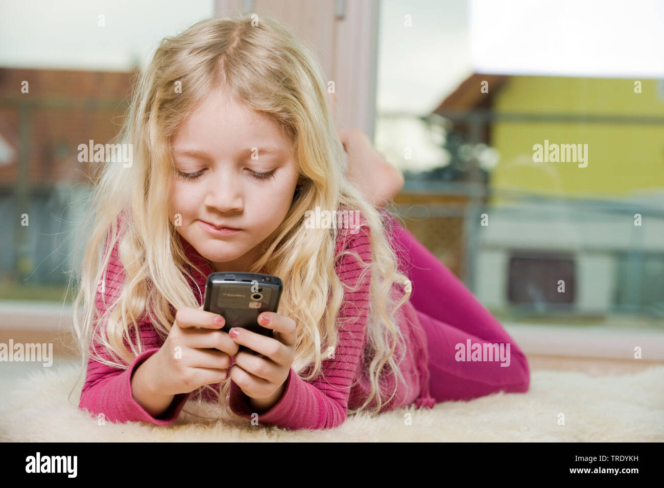 Portrait d'une fille allongée sur le sol et en jouant avec son téléphone portable Banque D'Images