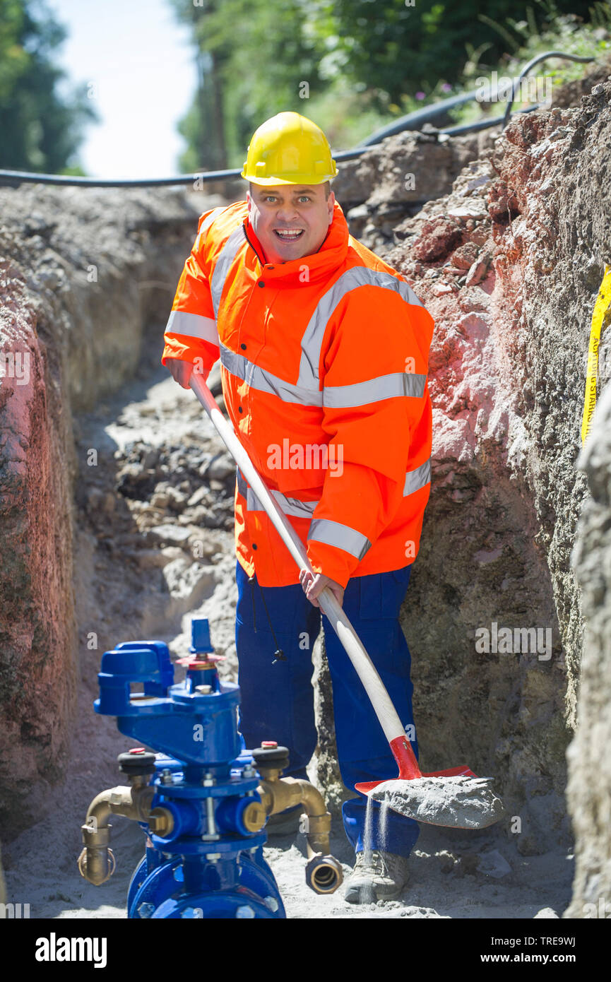 Travailleur de la construction d'une veste haute visibilité orange, pelleter du sable dans une tranchée d'excavation Banque D'Images