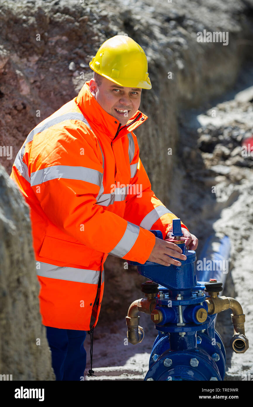 Travailleur de la construction d'une veste haute visibilité orange, travailler sur un bloc d'eau vanne dans une tranchée d'excavation Banque D'Images