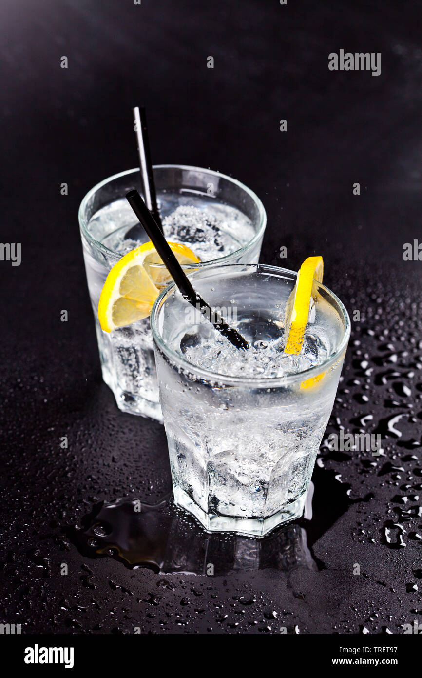 Deux verres d'eau gazeuse fraîche avec des glaçons et des rondelles de citron. L'eau de soude sur fond noir mouillé. Banque D'Images