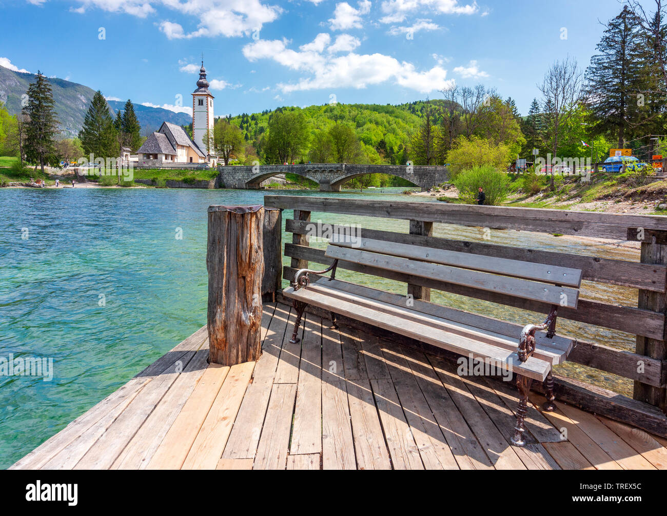 Banc de repos vith vie de l'église Saint Jean-Baptiste au lac de Bohinj, en Slovénie. Endroit idéal pour se reposer dans un paysage de printemps beautyful à eaux claires o Banque D'Images