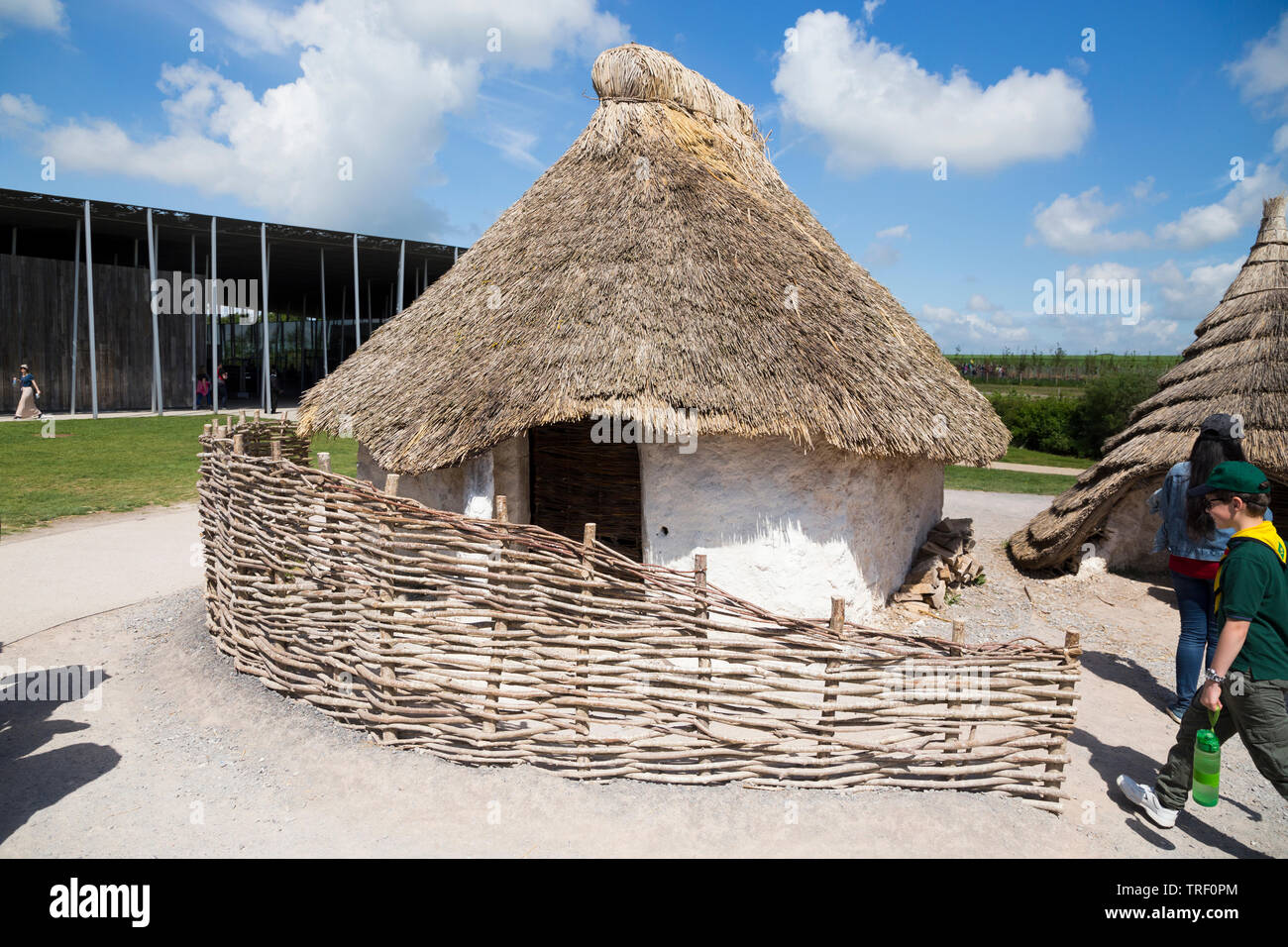 L'extérieur de l'âge de pierre néolithique recréé hut / huttes au toit de chaume stoneage / toiture tandis que les touristes se promener. Centre d'exposition du village ; Stonehenge / Stone Henge. Amesbury, Wiltshire, Royaume-Uni (109) Banque D'Images
