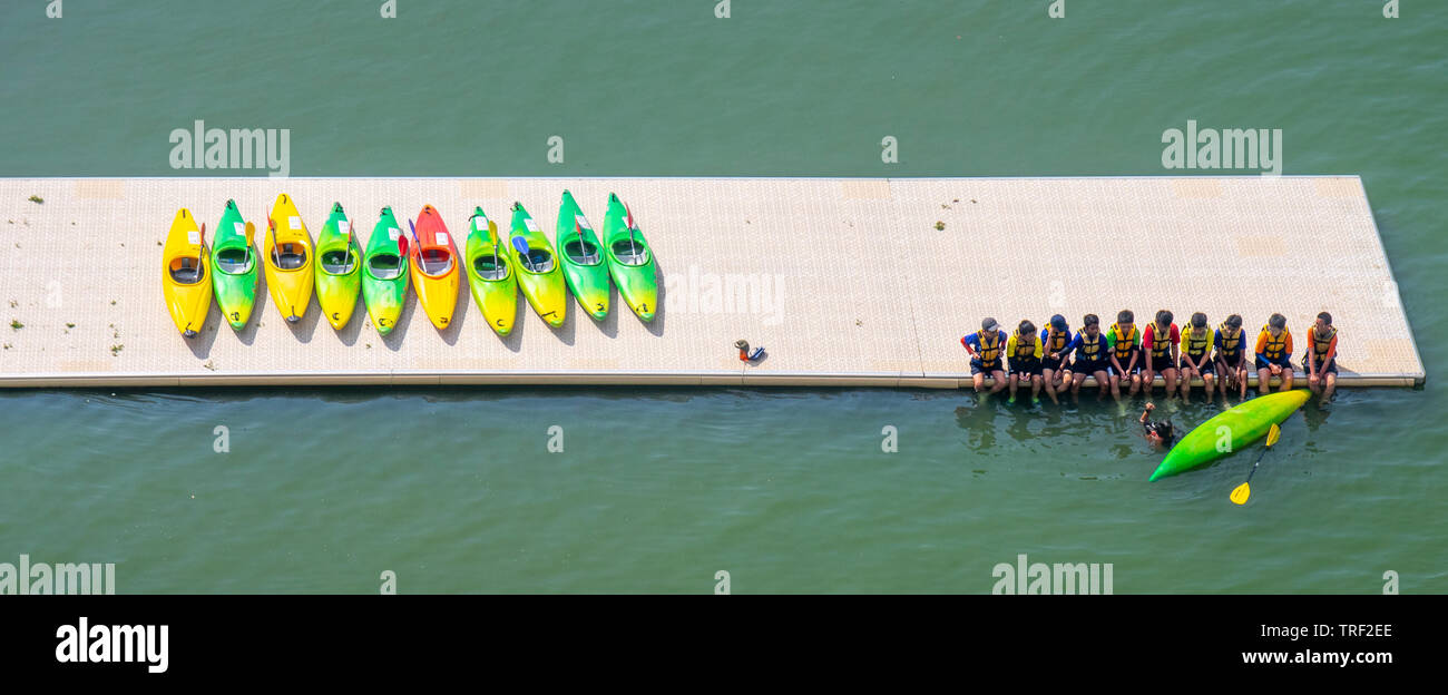Rangée de kayaks sur un ponton et une rangée de garçons assis sur le bord du ponton, les pieds dans l'eau. Banque D'Images