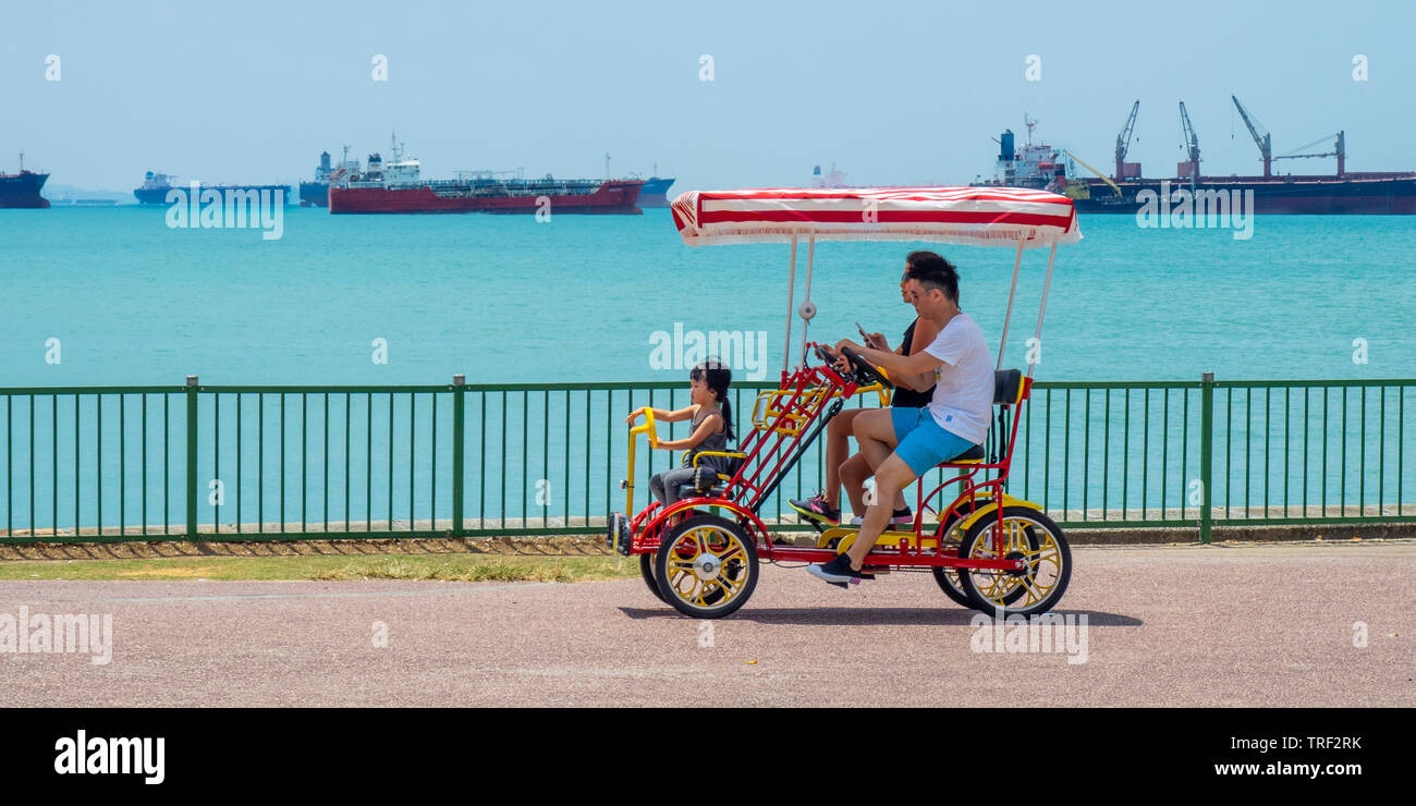 Une famille de voitures quadracycle le long de East Coast Park, cargos dans l'arrière-plan de Singapour. Banque D'Images