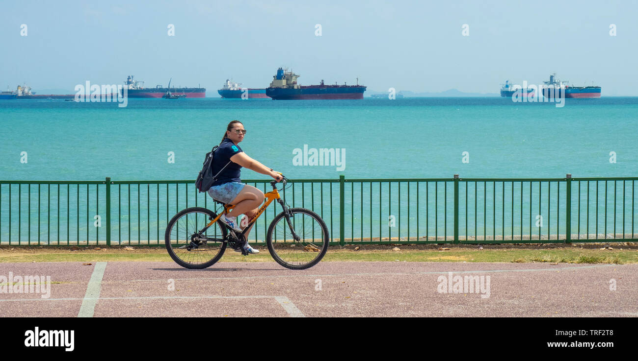 Loisirs équitation cycliste féminin son vélo le long d'East Coast Park, cargos dans l'arrière-plan de Singapour. Banque D'Images