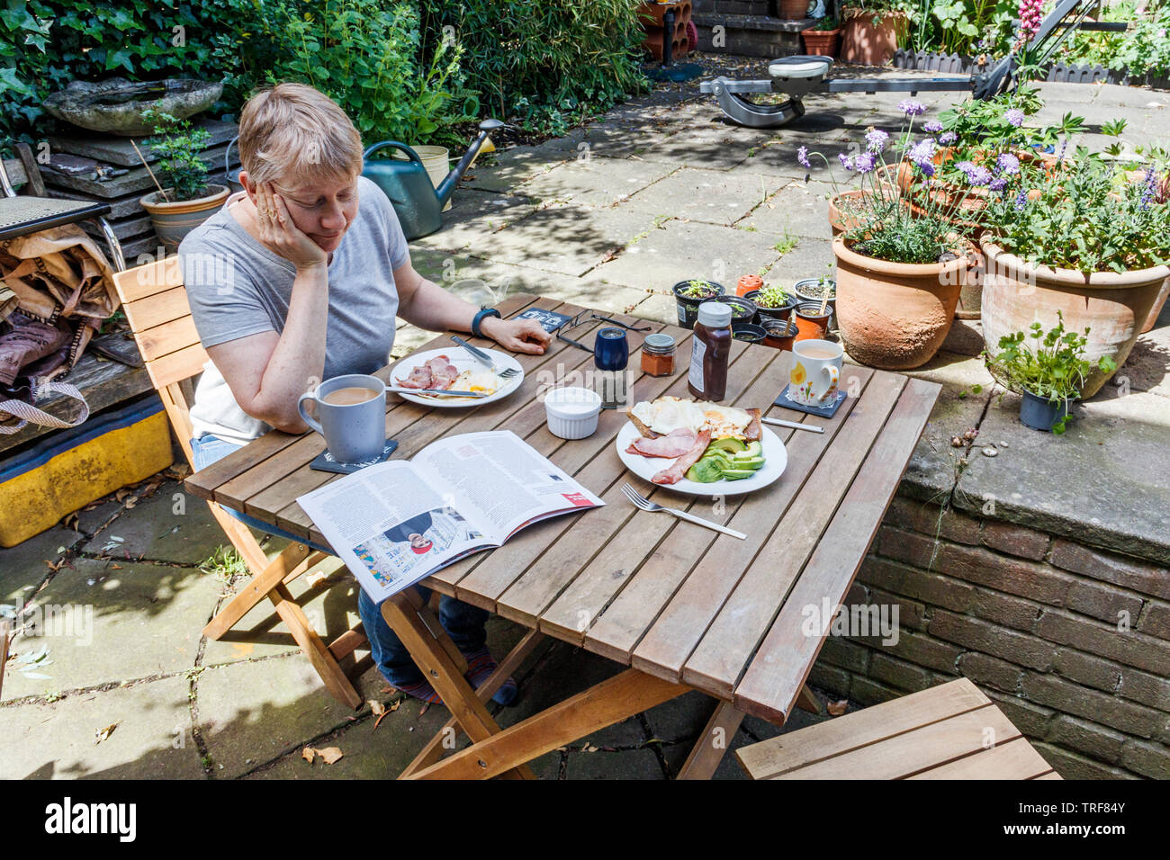 Une femme bénéficiant d'un petit déjeuner en plein air sur un patio jardin sur un beau matin d'été, Londres, UK Banque D'Images