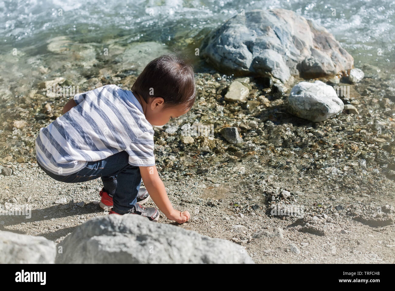 Une balade tout-petit ou l'enfant à la découverte par le fleuve, d'essayer de récupérer des rochers près de l'eau. Banque D'Images