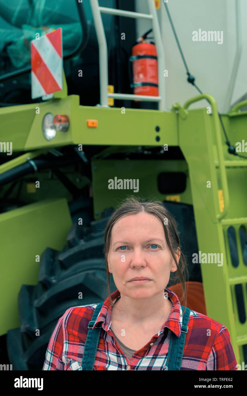 La productrice posant devant la moissonneuse-batteuse. Femme sérieuse travailleuse agricole avec les machines agricoles prêt faire les récoltes. Banque D'Images