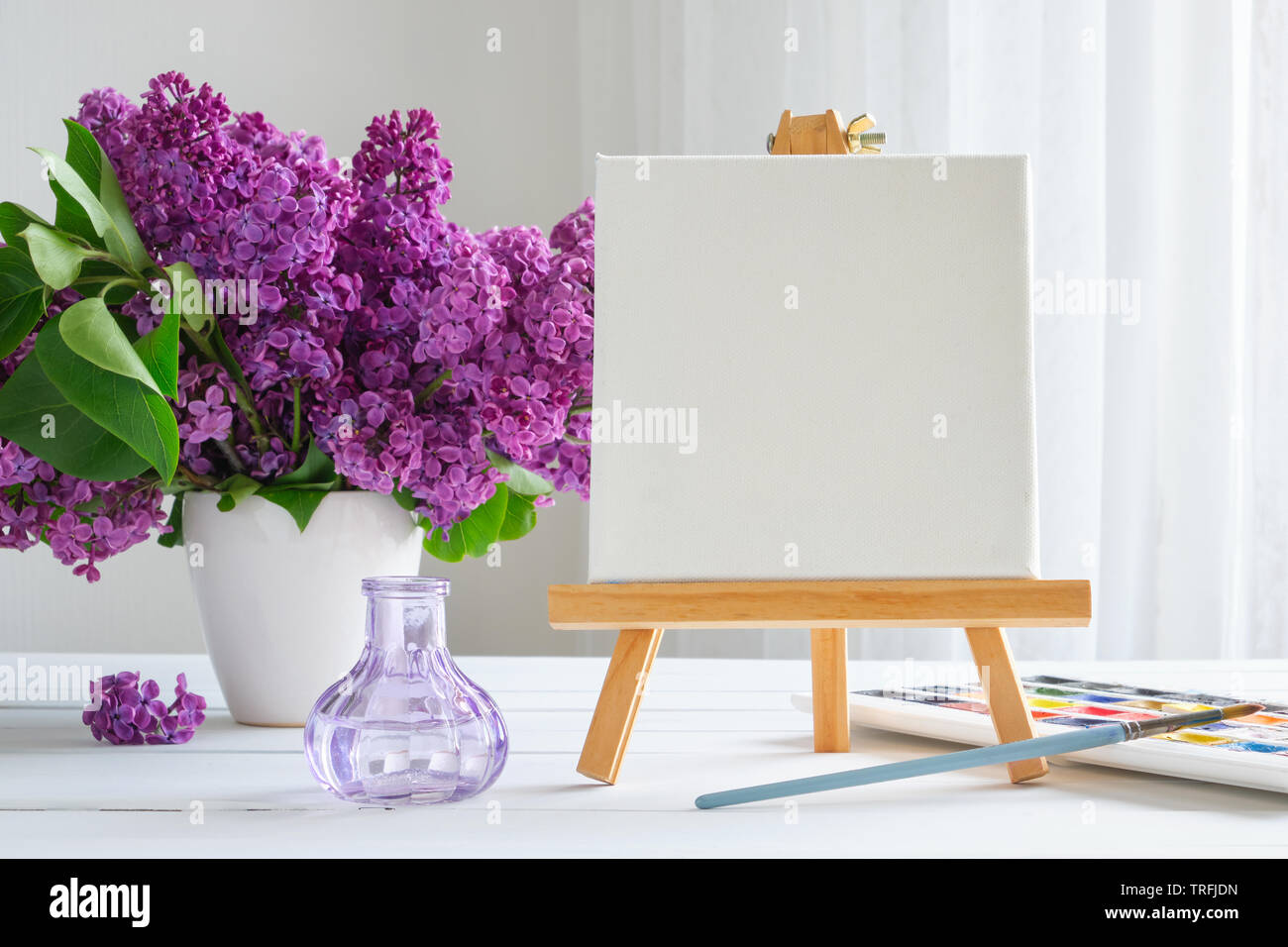 Toile blanche sur les peintures de chevalet, aquarelle, pinceau pour peindre et lilas fleurs sur table. Banque D'Images
