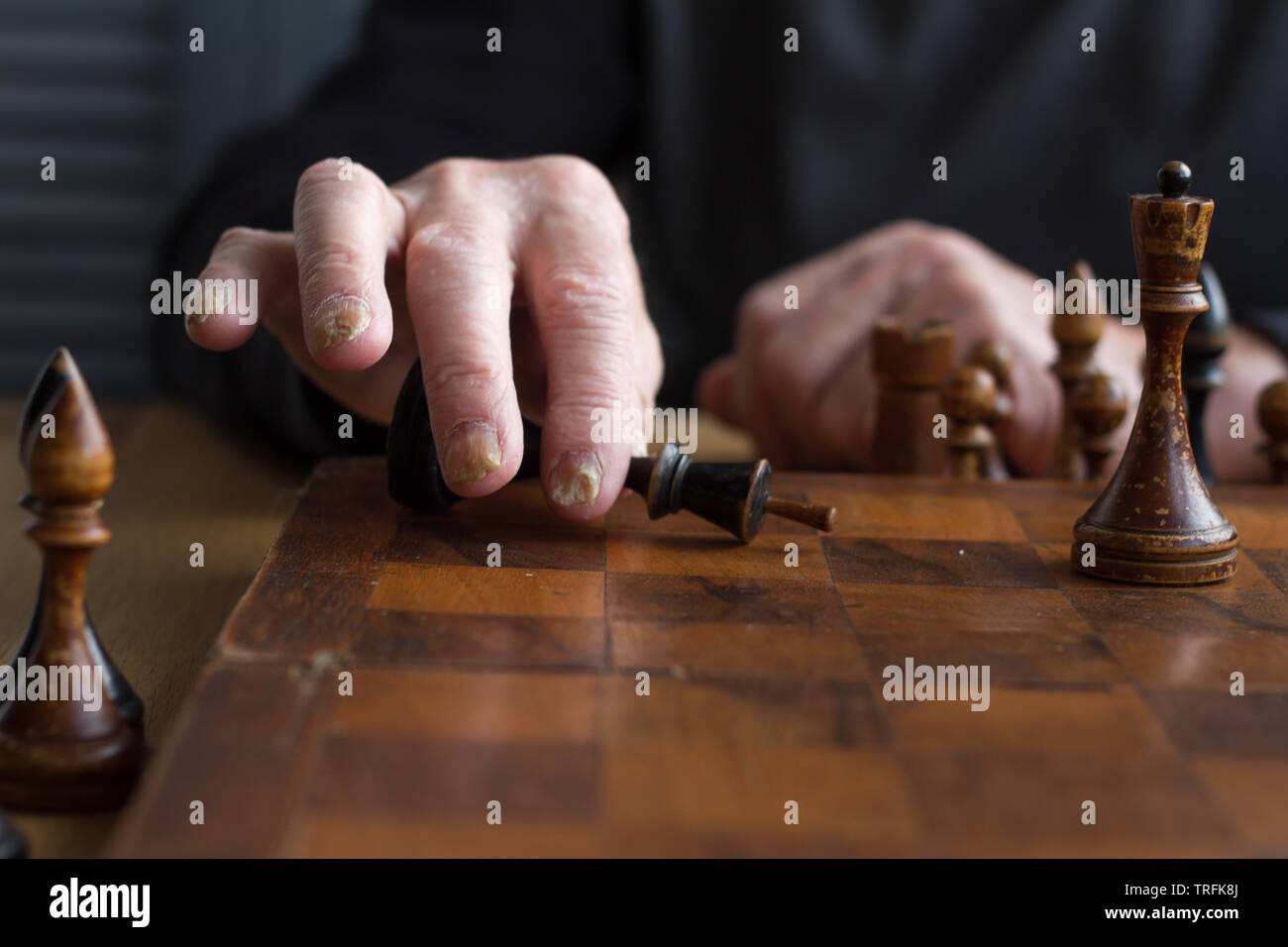 La main d'un vieil homme met une figure du roi noir sur le conseil reconnaissant la perte, jeux d'entreprise concept, selective focus, copyspace Banque D'Images