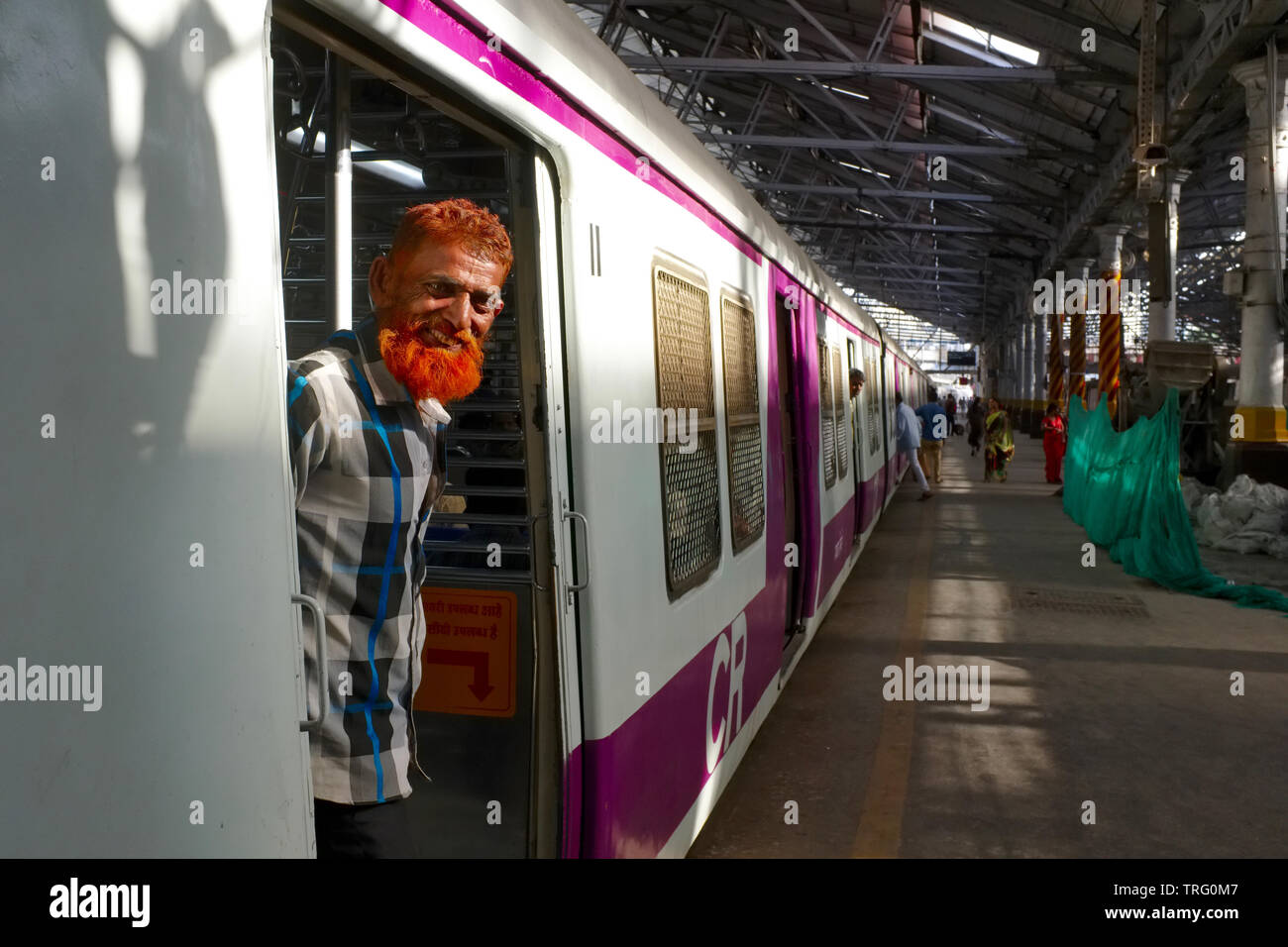Un musulman avec une barbe et des cheveux de couleur henné, debout à la porte d'un train de surburban à Chhatrapati Shivaji Maharaj Terminus à Mumbai, en Inde Banque D'Images