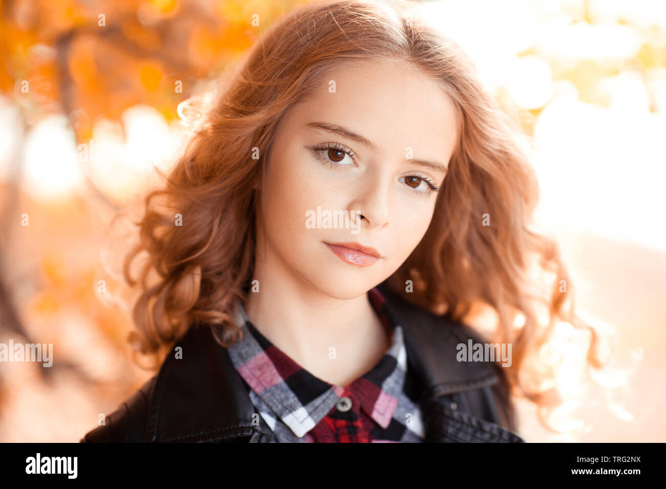 Belle fille blonde avec de longs cheveux bouclés 12-14 ans portant veste élégante en plein air au cours de l'automne nature background. En regardant la caméra. Banque D'Images