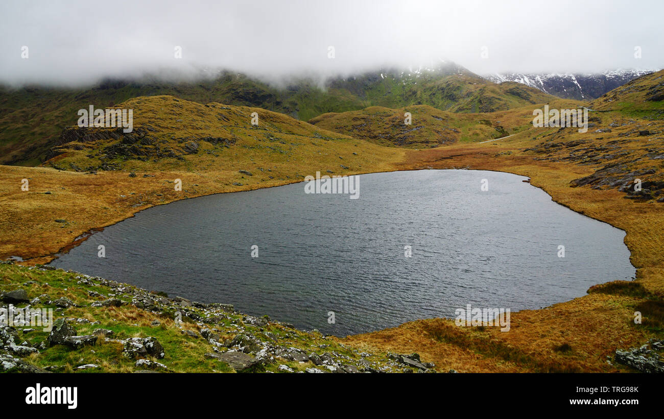 Beau, calme et paisible lac avec mystic et moody skies à l'arrière - capturés au cours d'une randonnée à Snowdon en hiver (Parc National de Snowdonia, Wale Banque D'Images