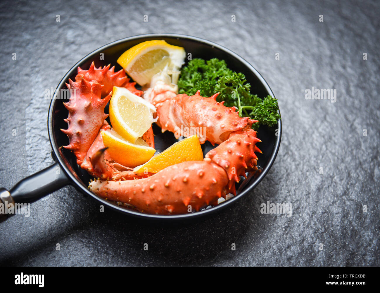 Pinces de crabe bouilli de fruits de mer cuit avec du crabe royal d'Alaska pan avec du citron persil herbes et épices sur fond sombre / crabe rouge hokkaido dans un pot chaud Banque D'Images