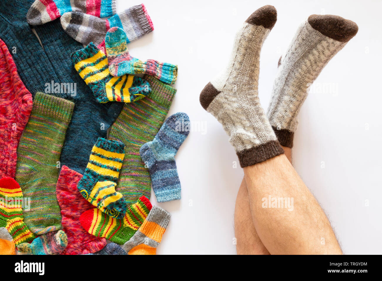 Vue de dessus d'un assortiment de chaussettes de laine de différentes tailles sur fond blanc avec une paire de pieds portant des chaussettes marron gris Banque D'Images