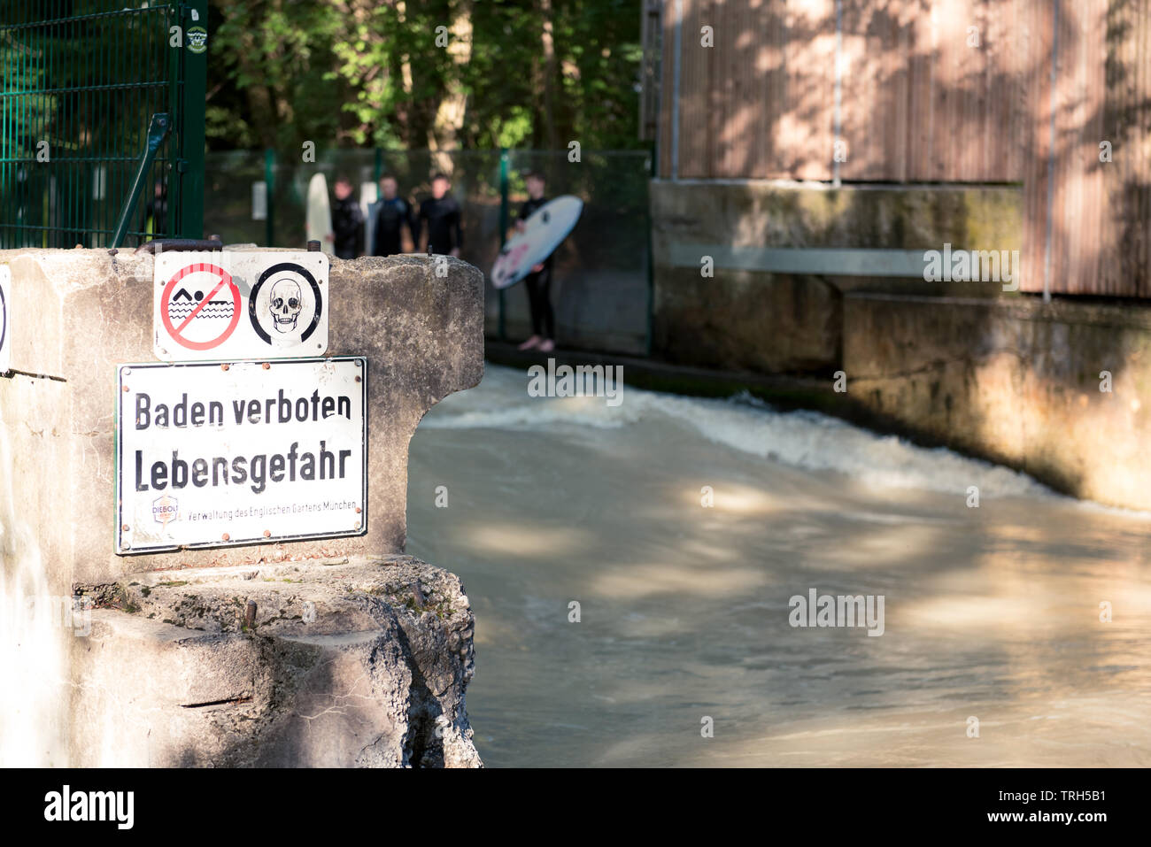 Surfers mâles sur la rivière Isar qui traverse le Jardin Anglais de Munich, en Allemagne avec des panneaux d'avertissement. Banque D'Images