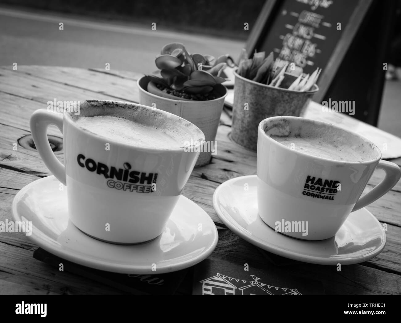 Deux tasses de café de Cornouailles sur une table en bois avec panneau de menu en arrière-plan en noir et blanc Banque D'Images Deux tasses de café de Cornouailles sur une table en bois avec panneau de menu en arrière-plan en noir et blanc Banque D'Images