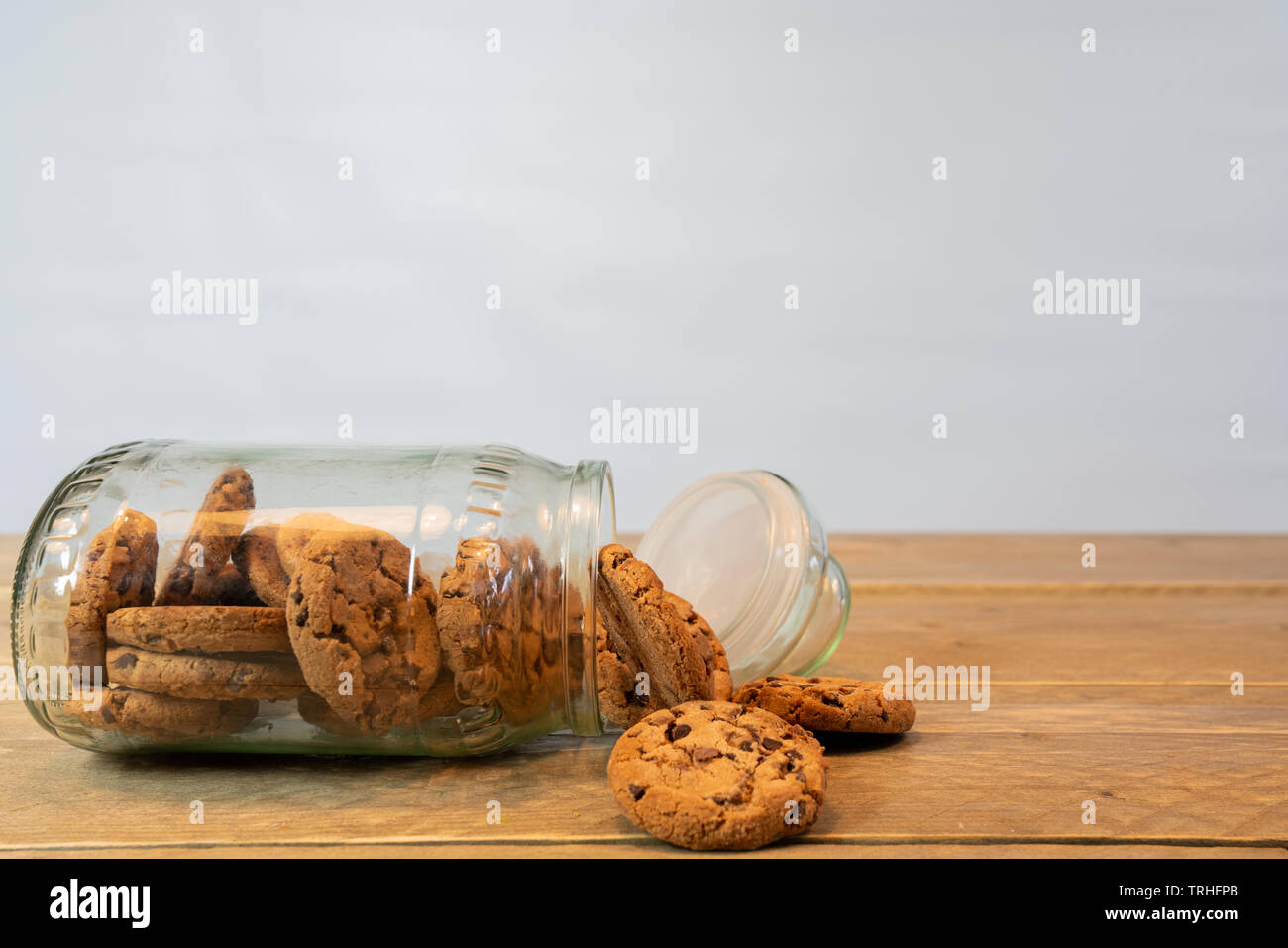 Pot en verre avec des cookies aux pépites de chocolat de son côté. Les cookies du pot sur la table en bois. Fond blanc Banque D'Images