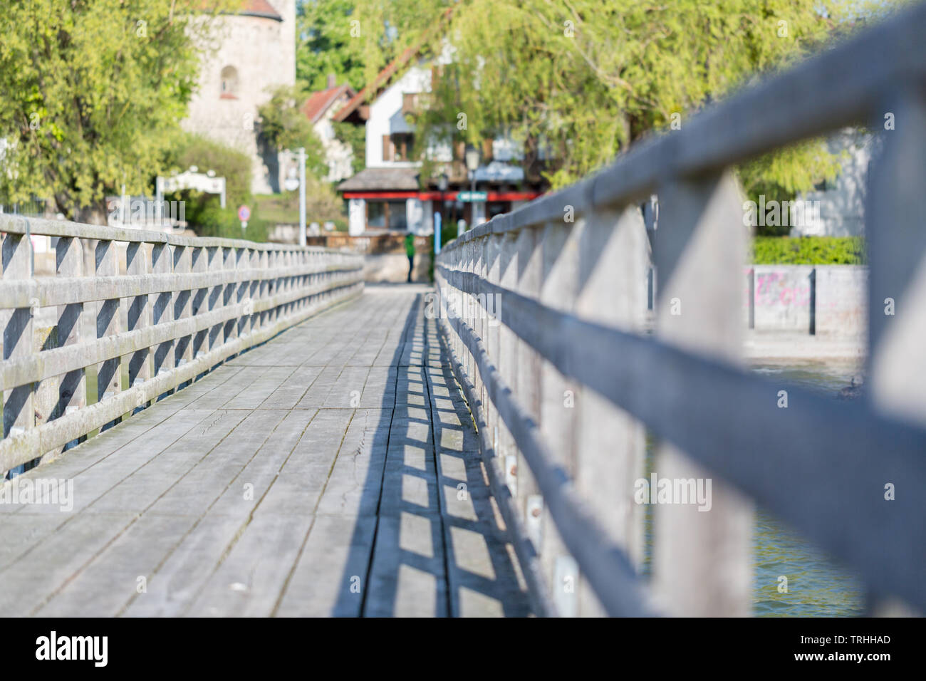 Low angle view of a landing stage / pier au lac Ammersee. Face à terre. Rampes en bois sur la gauche et droit. Arbres et maisons en arrière-plan. Banque D'Images