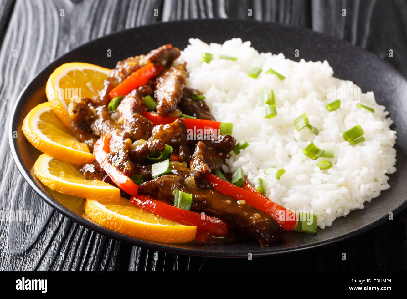 Pavé de boeuf asiatiques frit avec des poivrons dans le soja sauce à l'orange servi avec du riz sur une plaque horizontale sur la table. Banque D'Images