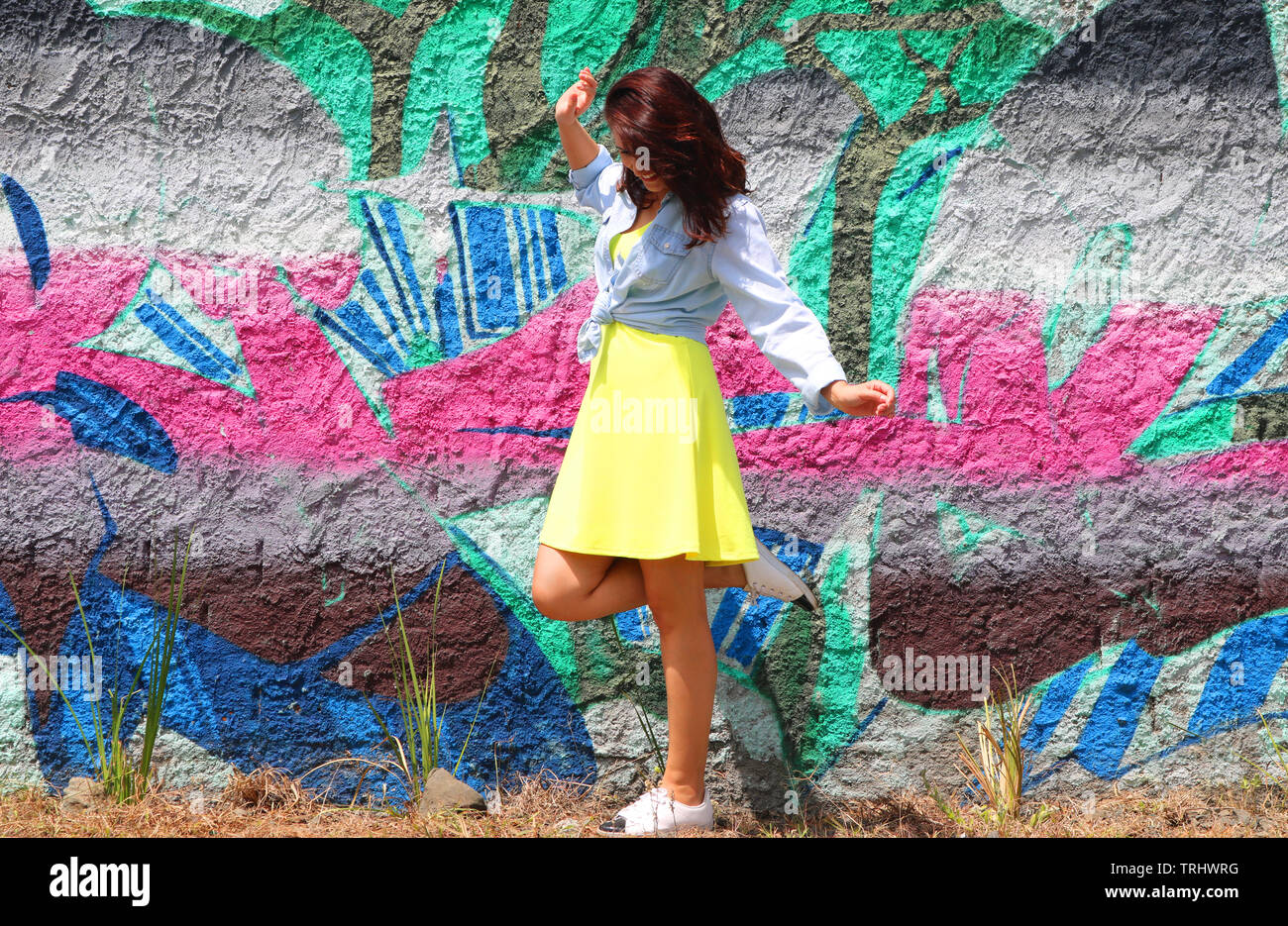 Silhouette de femme en robe jaune jeans et chemise en face d'un panneau de graphite dans un look street style avec un blanc sneakers et on éleva les pieds. Banque D'Images