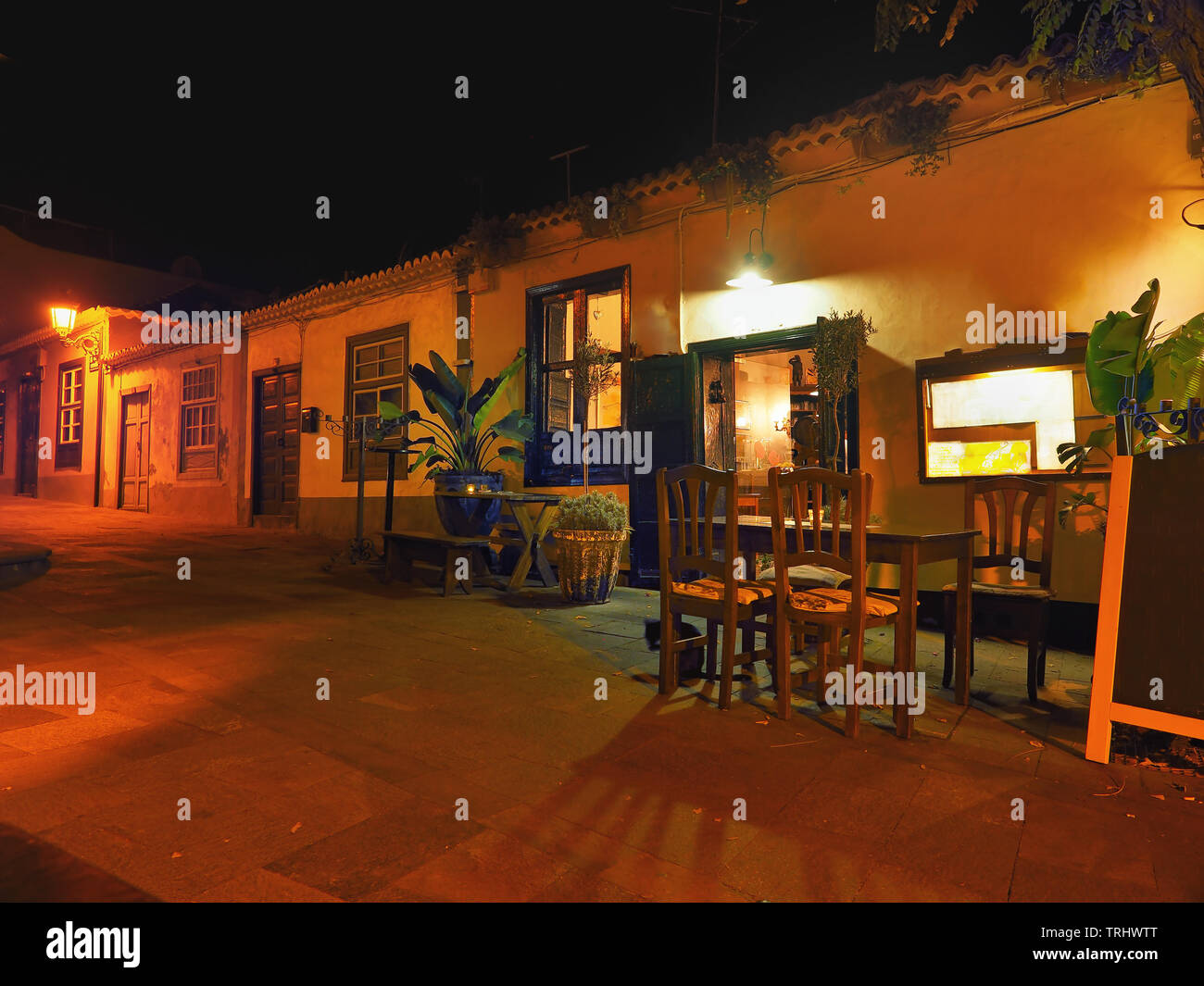 Une allée éclairée d'or doucement dans la nuit. Au premier plan sur le trottoir table et chaises en bois d'un Guachinche, un petit eatery Banque D'Images