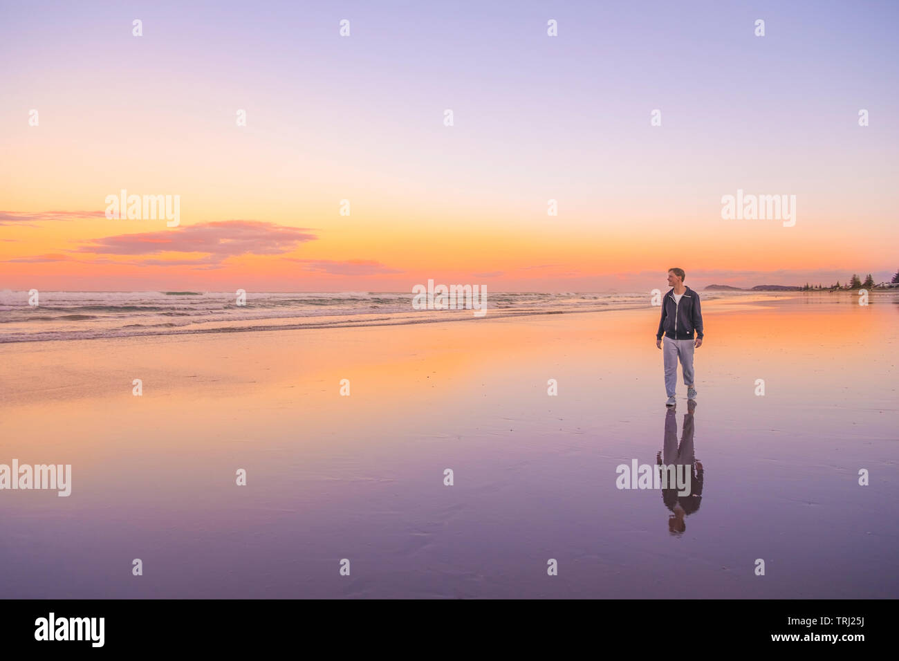 Un homme marche le long du rivage au coucher du soleil à Waihi Beach, New Zealand Banque D'Images