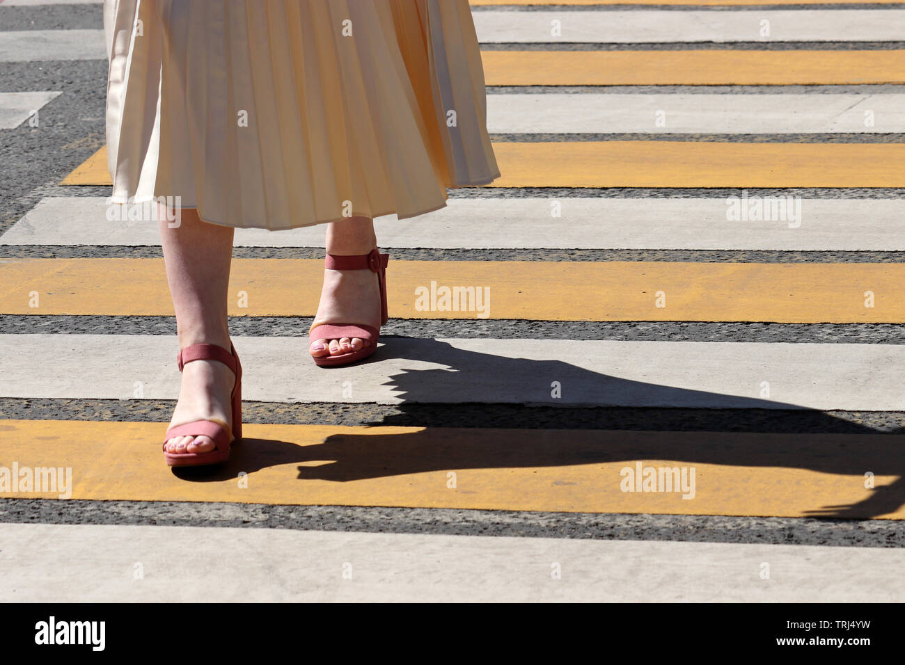 Femme dans une robe d'été et des chaussures à talons hauts marche sur passage piétons, l'ombre sur la moule. Marquage routier, les jambes sur le tableau de concordance Banque D'Images