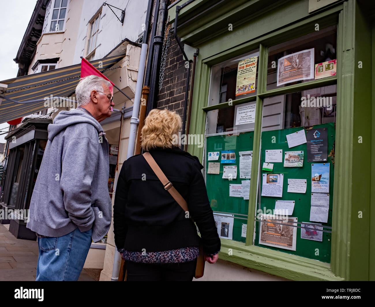 North Walsham, Norfolk, Royaume-Uni. 18 mai 2019. Photos de la rue franche - un vieux couple, un homme dans un sweat gris et un jean bleu et une dame dans un manteau noir, la lecture petites annonces locales dans la fenêtre d'un petit magasin dans High Street North Walsham Banque D'Images