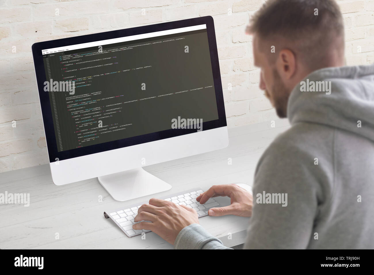 Codage homme app sur un ordinateur. Close-up scène. Office propre bureau avec mur de brique en arrière-plan. Banque D'Images
