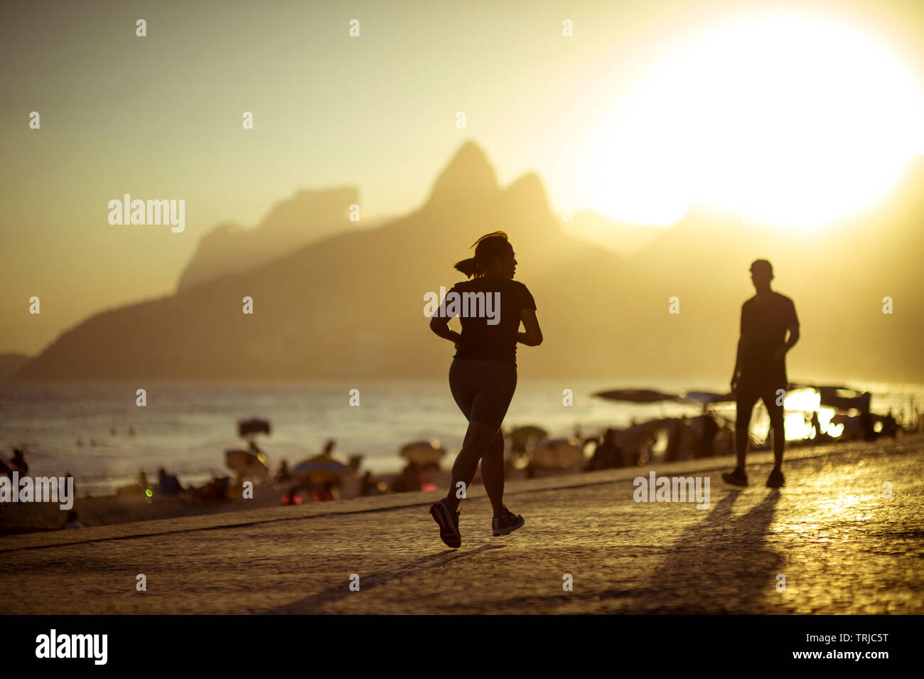 RIO DE JANEIRO - Mars, 2018 : les coureurs et les piétons partagent l'Ipanema Beachn demande que le soleil se couche derrière la montagne Deux Frères. Banque D'Images