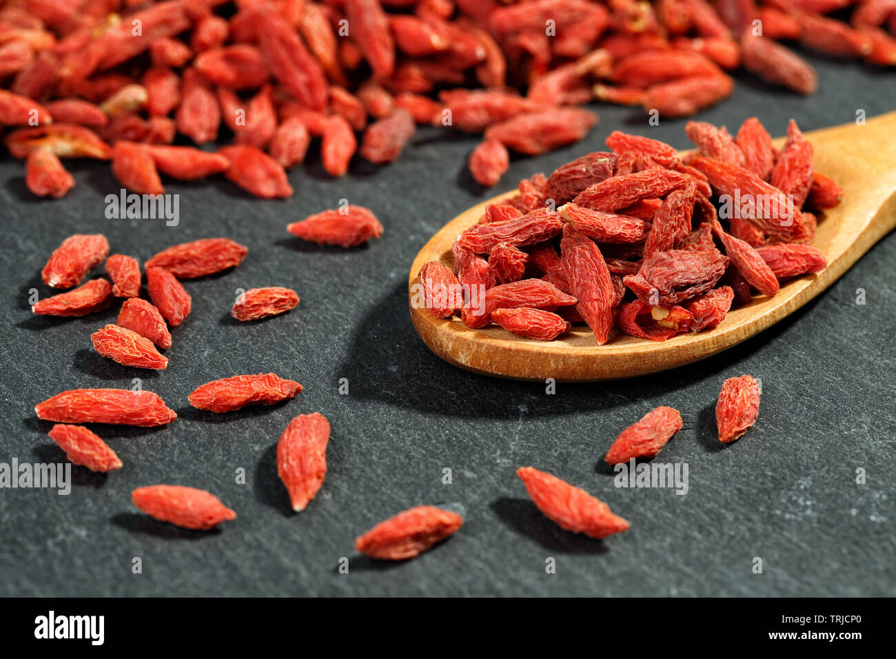 Extreme close up of dried goji bio (fruits) dans un wolfberries cuillère en bois sur une surface de la pierre noire. Texture Macro fond alimentaire Banque D'Images