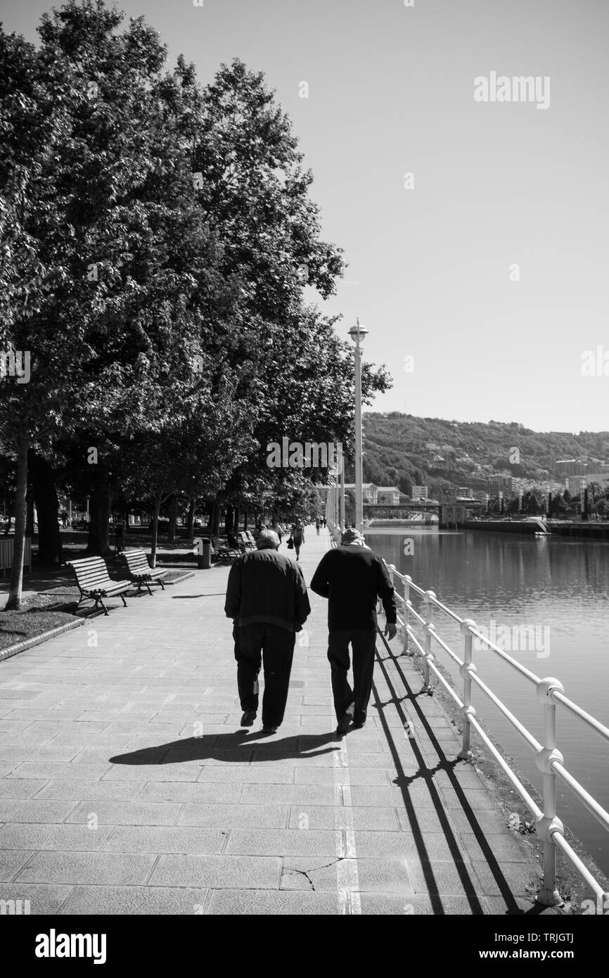 Deux hommes âgés marchant le long de la rivière sur une journée ensoleillée à Bilbao, en Espagne. Banque D'Images