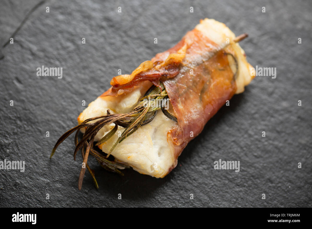 Un seul filet de lieu jaune cuit, Pollachius pollachius, qui a été mariné dans le jus de citron et l'ail écrasé avant d'être enveloppés dans du jambon de Parme Banque D'Images