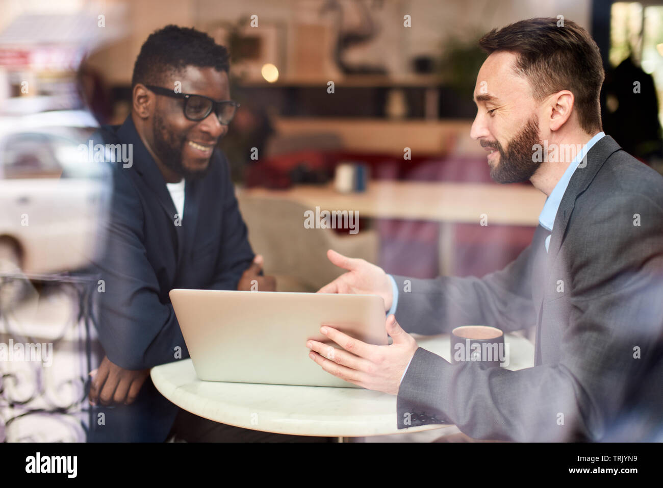 Deux hommes d'causacian et afro-américains ayant une conversation dans un café en face de l'ordinateur portable, à travers la fenêtre Banque D'Images
