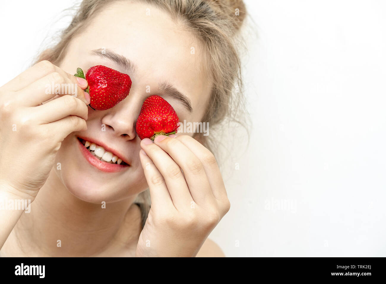 Les yeux de fraises . Belle Jeune femme tenant les fraises dans les yeux comme des jumelles. Mode de vie sain, concept. Banque D'Images