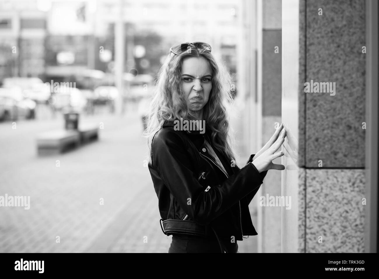 Fun grave triste femme blonde en manteau de cuir sur grimaçant rue looking at camera, monochrome Banque D'Images