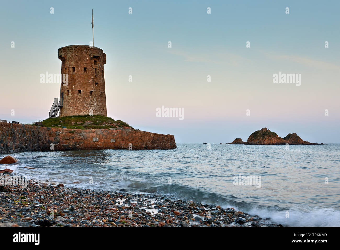 Image de la tour de Jersey, Jersey, la HOCQ Michaël Mobilis in Mobile au coucher du soleil avec des petites vagues et des pierres sur la plage. Banque D'Images